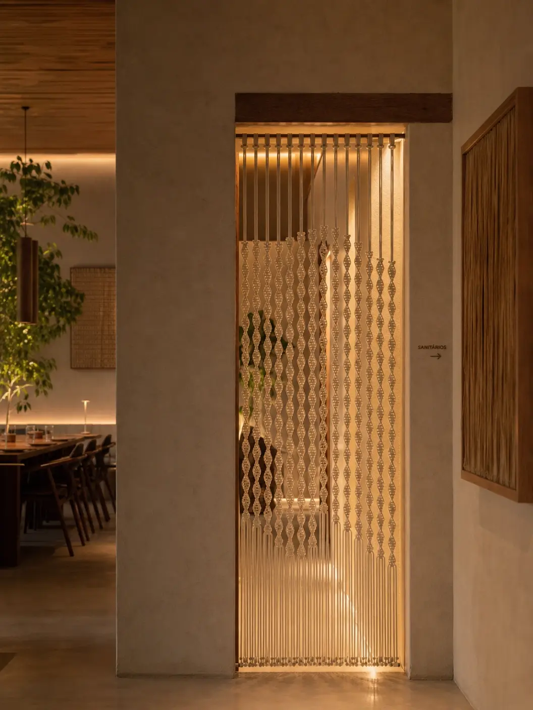 Divisor de macramê iluminado em corredor de restaurante com sinalização para sanitários